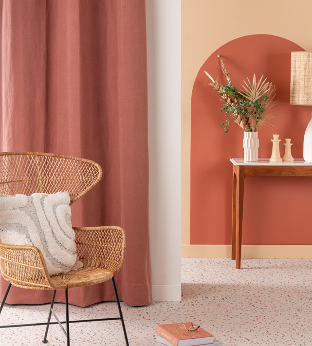 Mur terracotta avec arche peinte, console en bois et fauteuil en rotin, exemple de finition murale durable pour une extension.